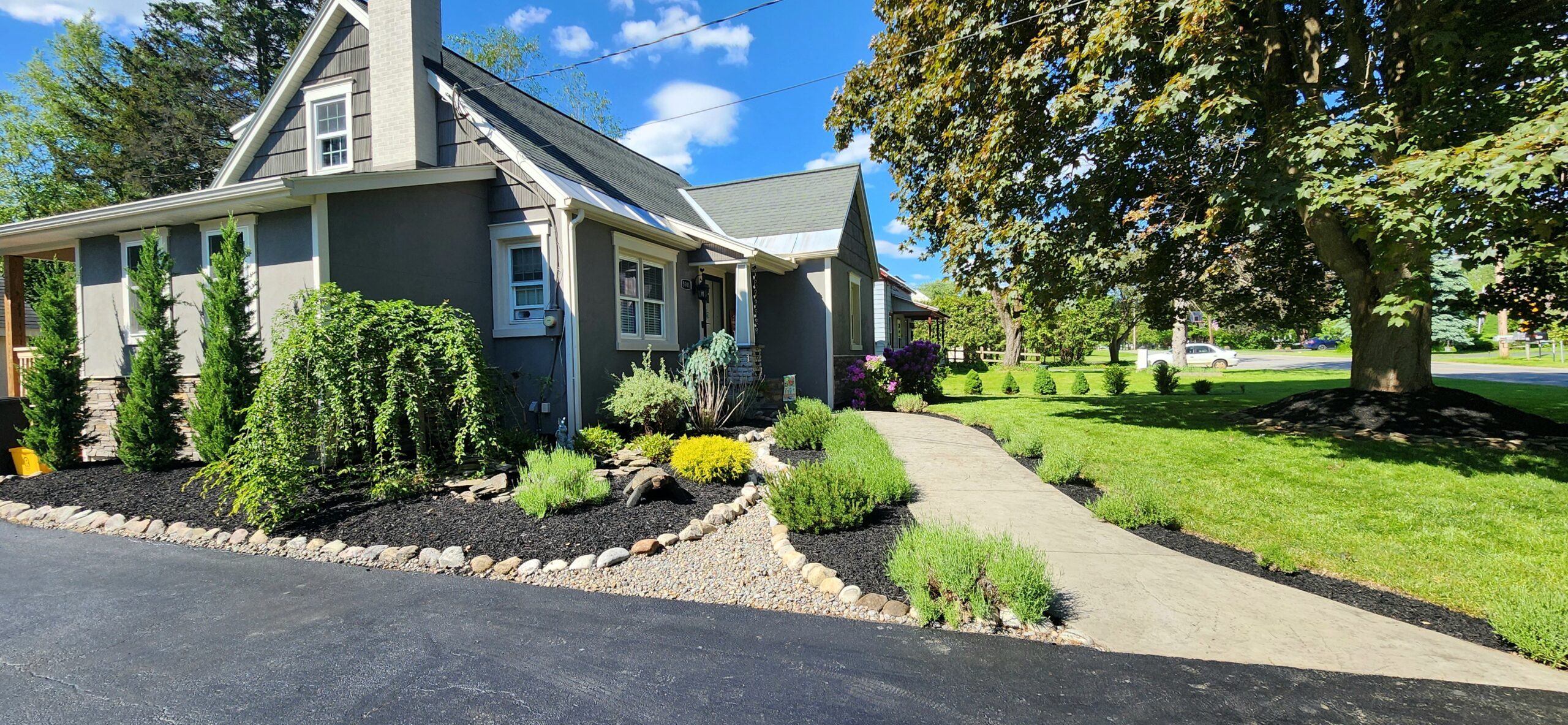 Fresh mulch in newly maintained landscape beds with shrubs and decorative stone dry river bed in front of a home in Utica, NY