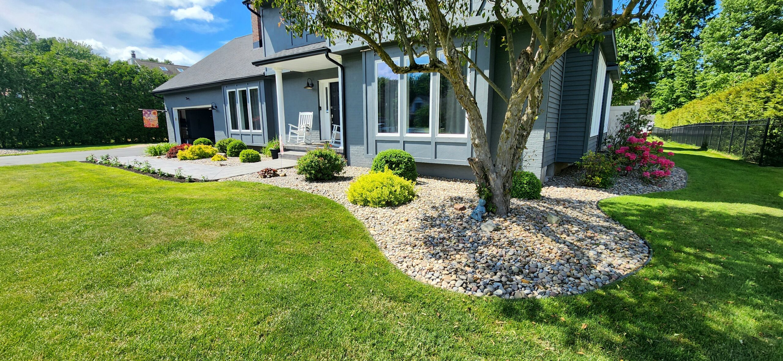 Beautifully installed landscape rock bed with fresh mulch and colorful shrubs around a mature tree in front of a home in New Hartford, NY
